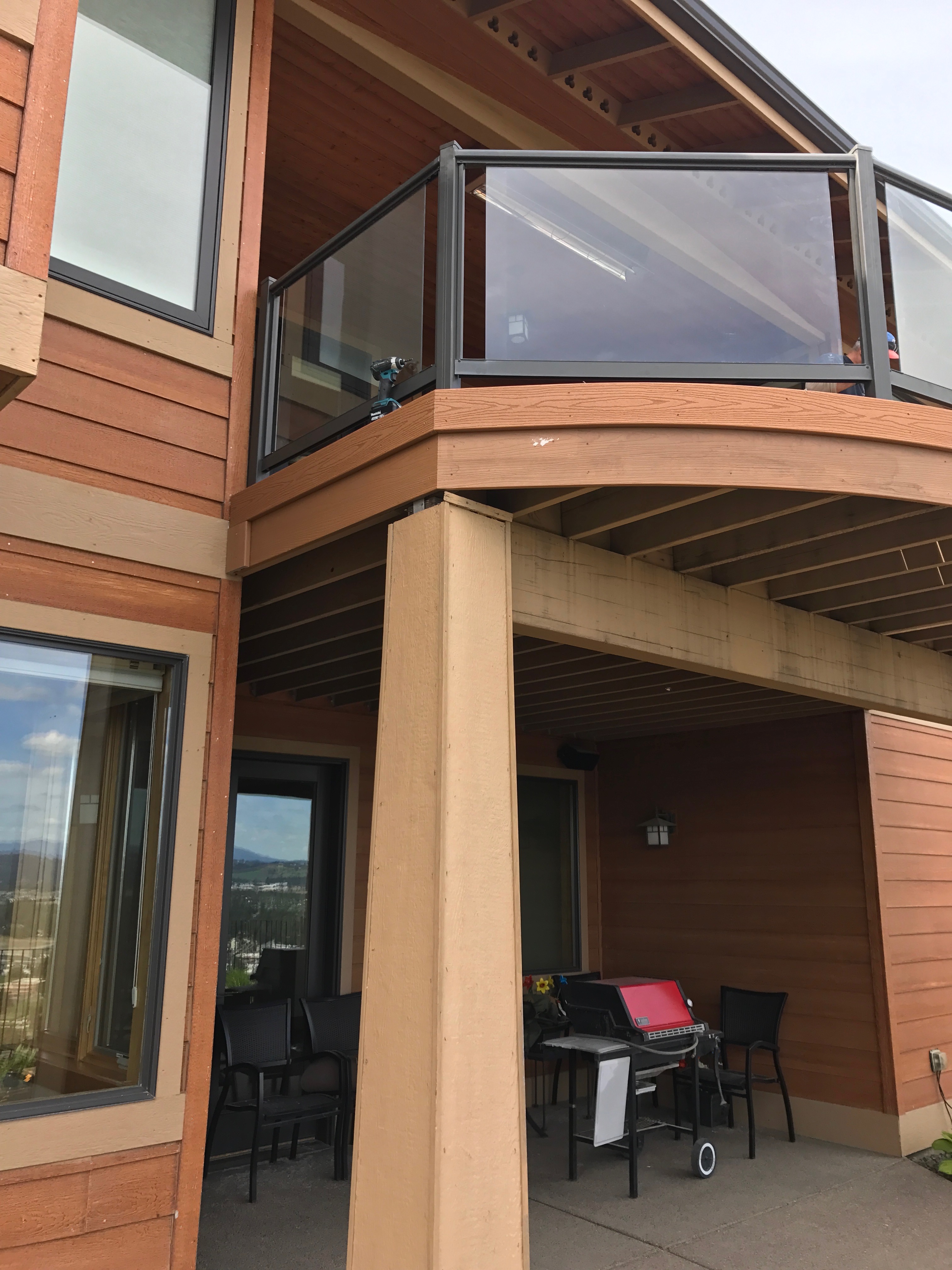 Second-story deck with curved glass railing and finished under-deck patio space with open beams.