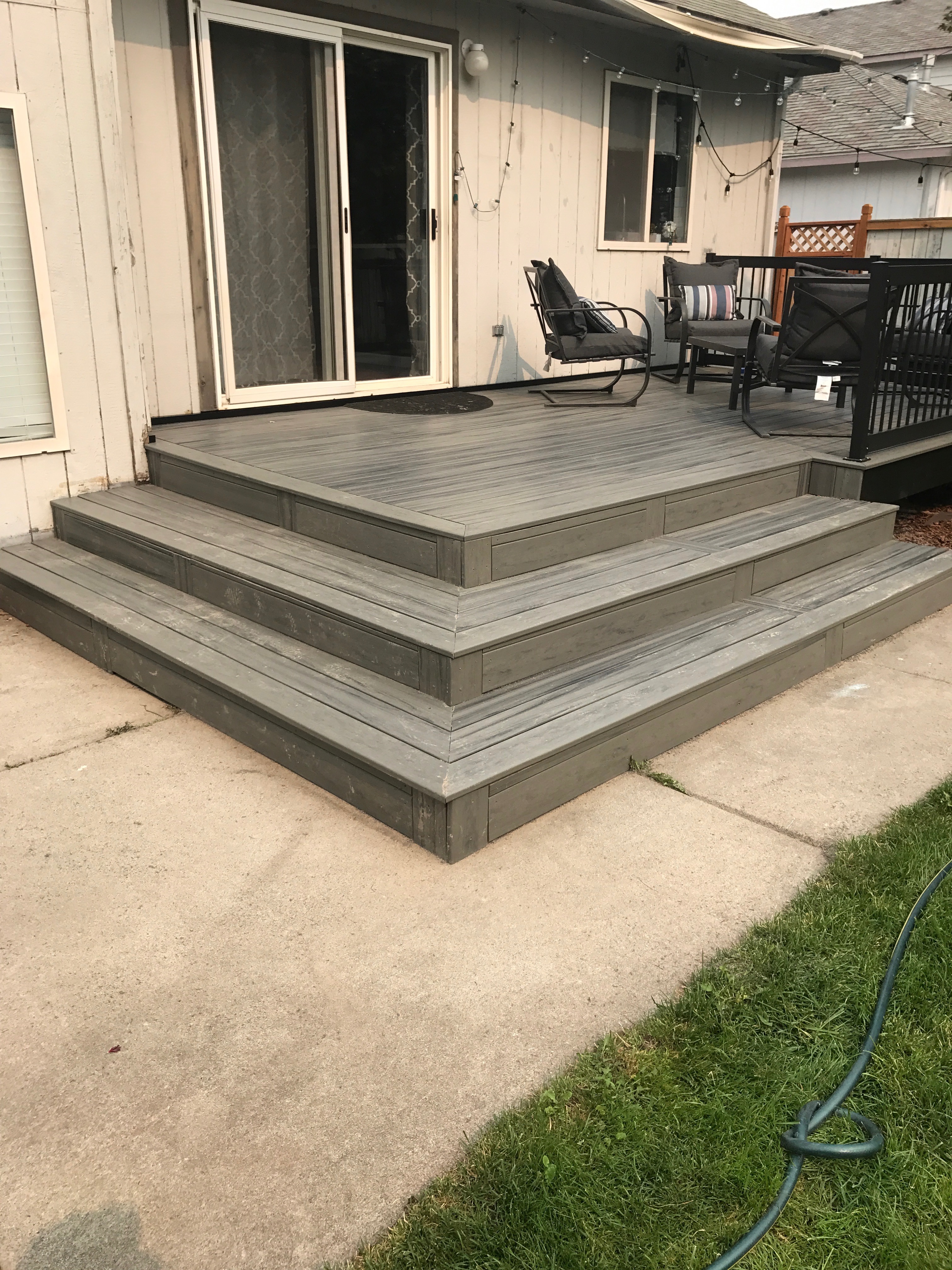 Grey composite deck with wide terraced steps leading to a backyard patio area.
