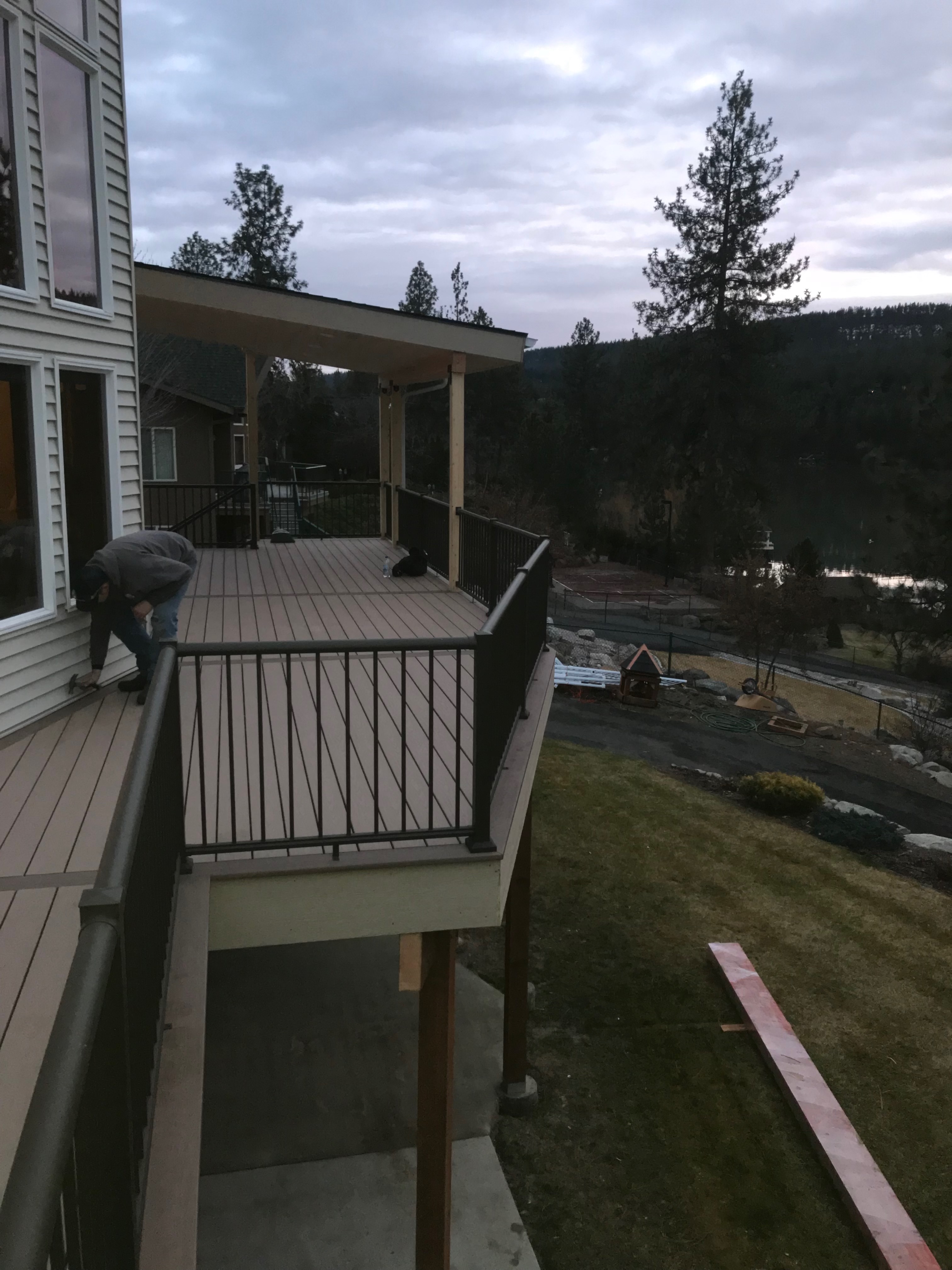 Elevated tan composite deck with black aluminum railing and covered structure overlooking a scenic hillside.